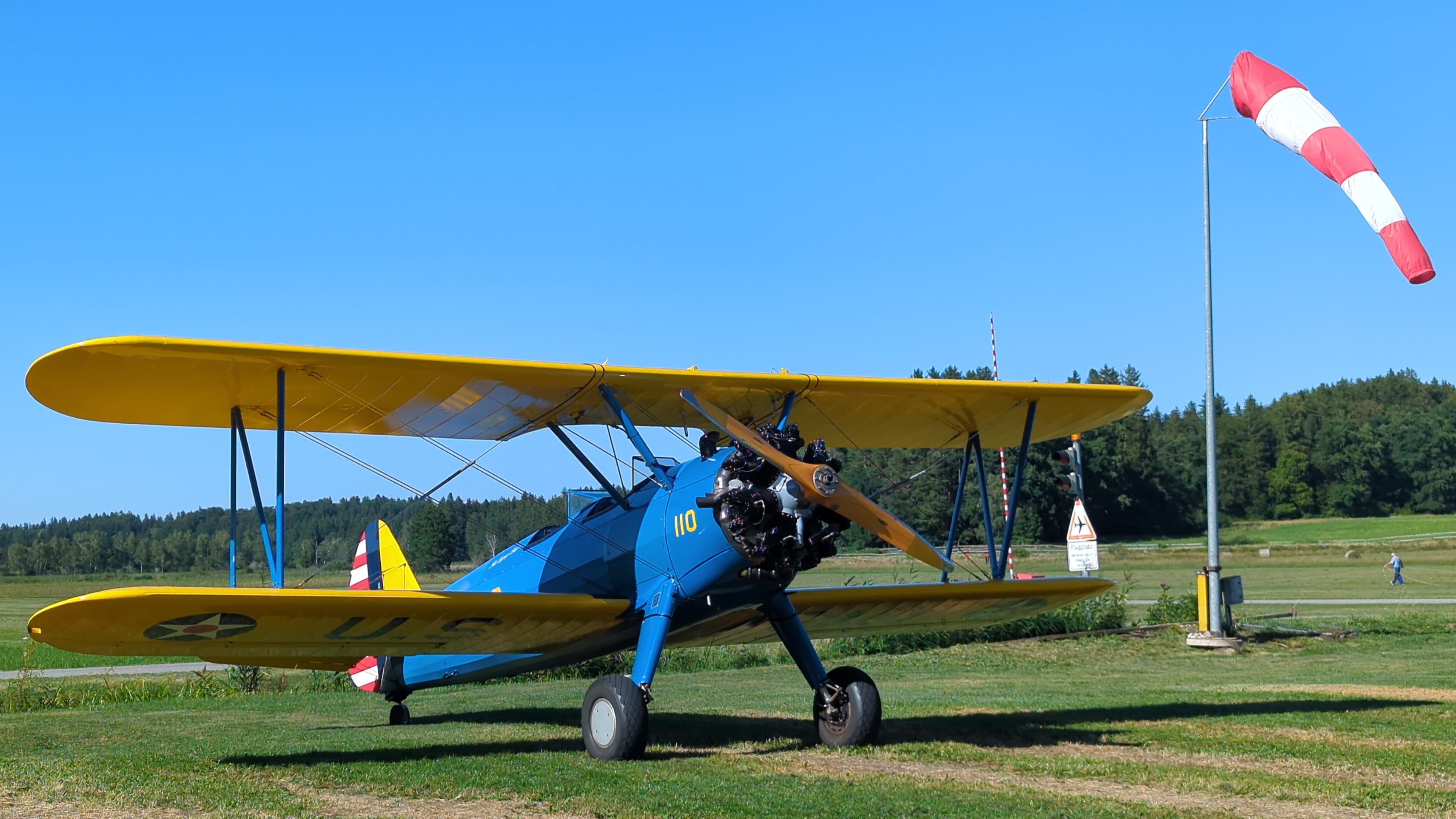 Boeing Stearman in blue and yellow next to windsock.